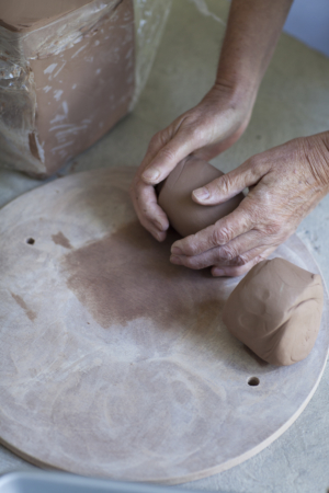 A block of soil, a pair of hand kneading some into a bowl, another bowl.
