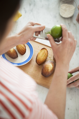 A person putting lime zests on madeleines placed on a chopping board.