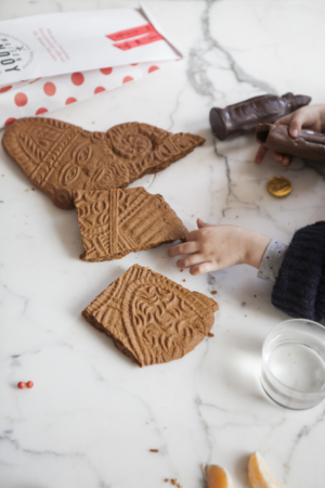 Kleine meisjeshanden die een chocolade Sinterklaas en stukjes van een speculoos van de Sint grijpen.