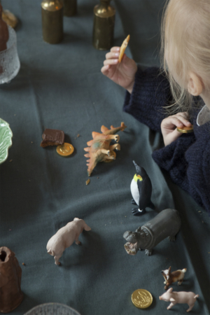 Klein meisje dat koekjes eet aan een tafel met dierenfiguurtjes.