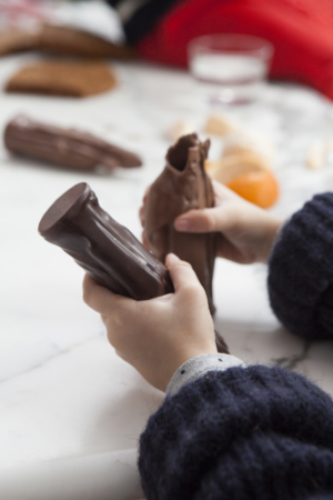 Kleine meisjeshanden die twee chocolade Sinterklaasjes vasthoudt, één donkere en één melkchocolade.
